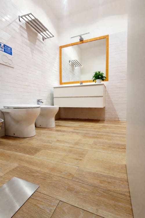Bagno moderno dell'appartamento Zoelia Roma con piastrelle bianche a metro, specchio con cornice arancione, mobile in legno, bidet e rivestimenti in legno