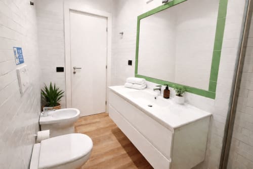 Bagno moderno a Zoelia Roma con piastrelle bianche, specchio con cornice verde, lavabo bianco e pavimento in legno