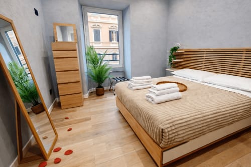 Camera moderna a Zoelia Roma con letto in legno, biancheria bianca, vista sulla città, specchio, cassettone, piante in vaso e pavimenti in legno