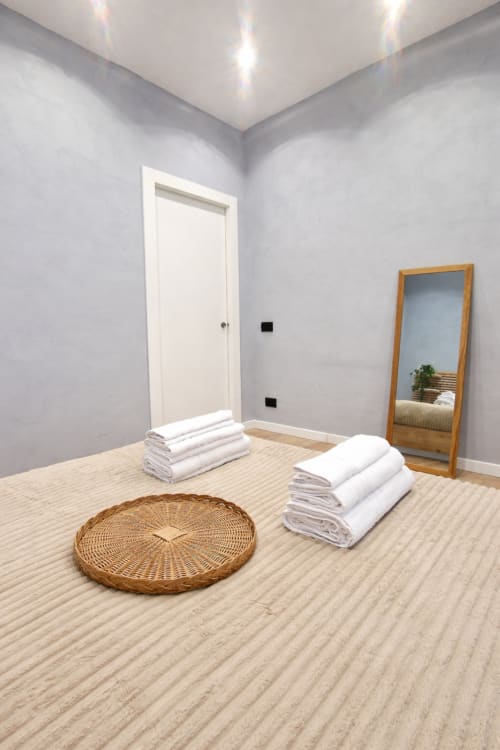 Camera minimalista dell'hotel Zoelia Roma con asciugamani bianchi, stuoia intrecciata, specchio in legno, pavimenti in legno chiaro e design moderno