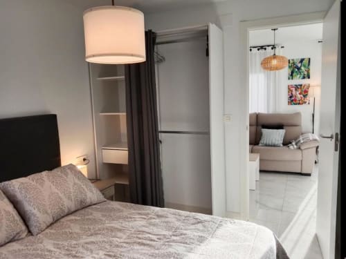 Dormitorio moderno en apartamento Top Home Integra en Jerez de la Frontera con lámpara colgante, espejo y vista a la sala de estar