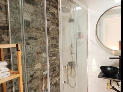 Baño moderno con ducha de piedra natural, lavamanos negro tipo vasija y espejo redondo en el apartamento Top Home Integra de Jerez de la