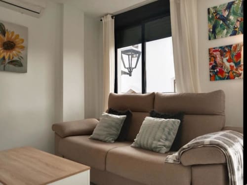 Acogedora sala de estar en Top Home Integra, Jerez de la Frontera, con sofá beige, cojines decorativos y vistas a la ciudad