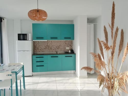 Moderna cocina turquesa con lámpara colgante de mimbre, electrodomésticos blancos y decoración de pampas secas en apartamento de Jerez