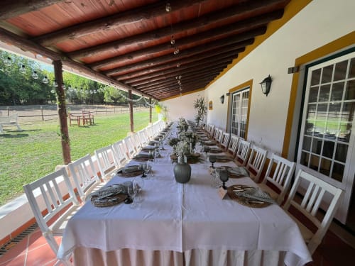 Mesa de jantar comprida preparada para evento sob pérgola na Quinta da Alcaidaria-Mór em Ourém, Fátima