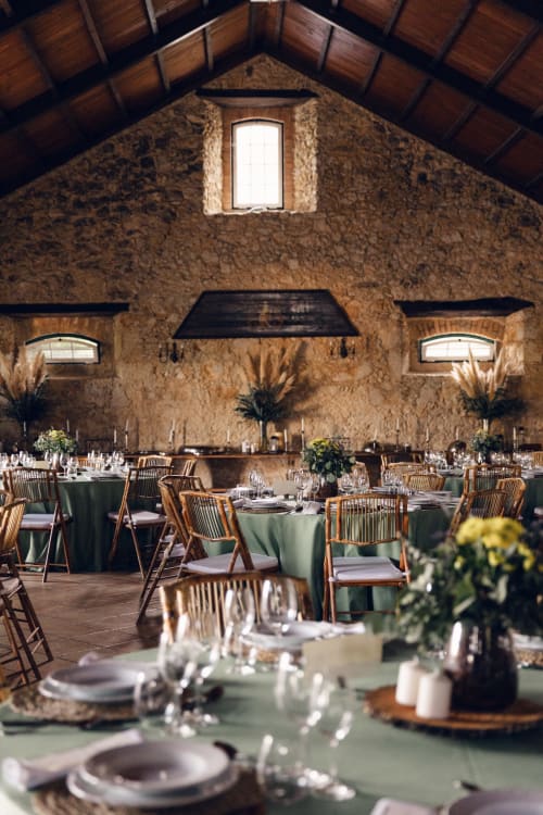 Rustic stone banquet hall at Quinta da Alcaidaria-Mór with elegant green tablecloths, wooden chairs, and candlelit tables set