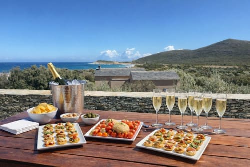 Installation élégante de champagne et d'amuse-bouches en plein air à la Villa Marine à Centuri, Corse, avec vue sur la mer Méditerranée