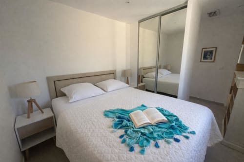 Chambre lumineuse de la Villa Marine à Centuri, avec lit, armoire miroir, châle turquoise et livre ouvert