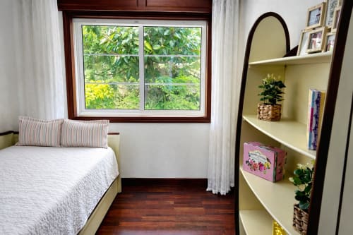 Dormitorio luminoso en apartamento Mariño, Baiona con ventana de marco de madera, almohada a rayas, estantería crema con plantas y piso de madera