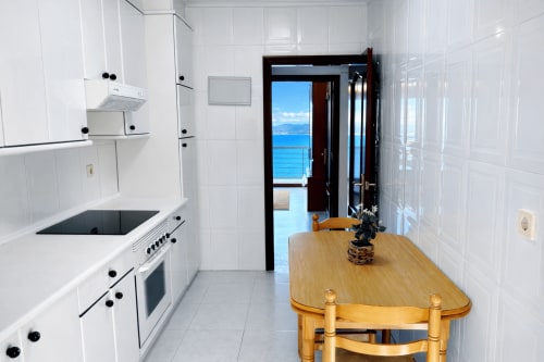 Cocina moderna con vista al mar en apartamento de Baiona, con muebles blancos, mesa de comedor de madera y vistas al océano
