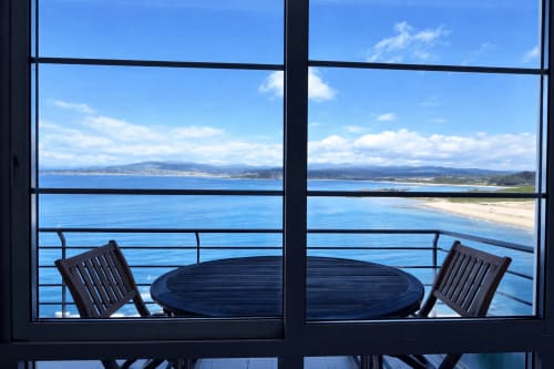 Terraza con vistas al mar de Baiona con dos sillas y mesa redonda frente a la playa y montañas