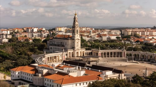 Basilica sanctuary in Fátima with white colonnade and bell tower, cityscape of Ourém in background