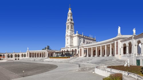 Sanctuary of Fátima basilica with white colonnade and bell tower under blue sky, near Quinta da Alcaidaria-Mór in Ourém,