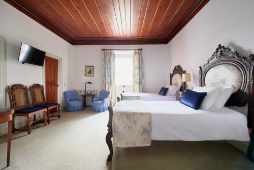 Elegant bedroom at Quinta da Alcaidaria-Mór with ornate wooden ceiling, period furniture, and two queen beds with blue