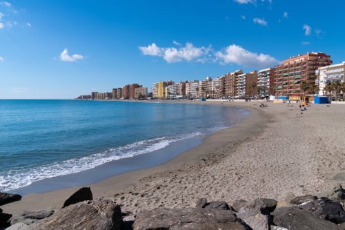 Playa de Málaga con arena blanca, mar Mediterráneo azul y edificios de apartamentos frente al mar bajo cielo despejado