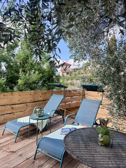 Terrasse extérieure d'Agritusmo Stecadò avec transats, olivier et vue sur le village de Dolceacqua, Italie