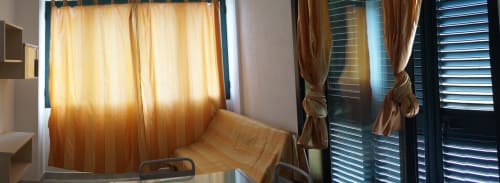 Bright apartment bedroom with yellow curtains, wooden chair, and shuttered doors in Orosei, Italy