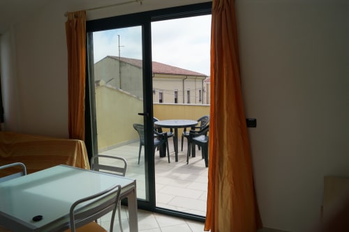 Orosei apartment veranda with city view, wooden table and chairs, modern glass doors opening to furnished balcony