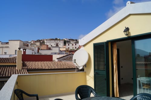 Sunny rooftop terrace with wooden chairs, satellite dish, and sea view overlooking Orosei village, Sardinia