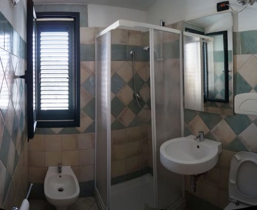 Modern bathroom in Orosei apartment with shower enclosure, dual sinks, and tiled walls with geometric patterns
