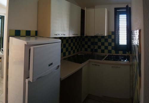 Compact kitchen in Orosei apartment with checkered backsplash, gas cooktop, refrigerator, and cream cabinets