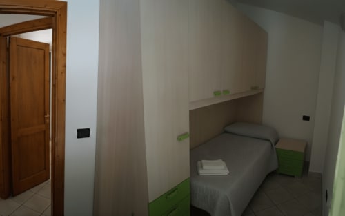 Compact bedroom in Sa Domo de Su Zeniu apartment, Orosei, with single bed, green accents, and wooden door entry