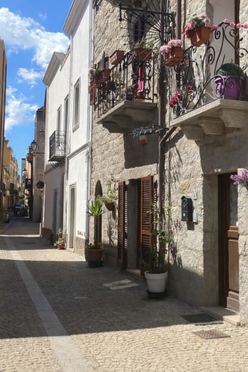 Affascinante vicolo lastricato a Olbia con edifici in pietra, balconi decorativi, fiori rosa e architettura mediterranea