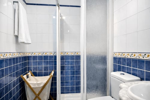 Baño moderno con acentos de azulejos azules, mampara de ducha de cristal y accesorios blancos en el apartamento Holibai, Baiona