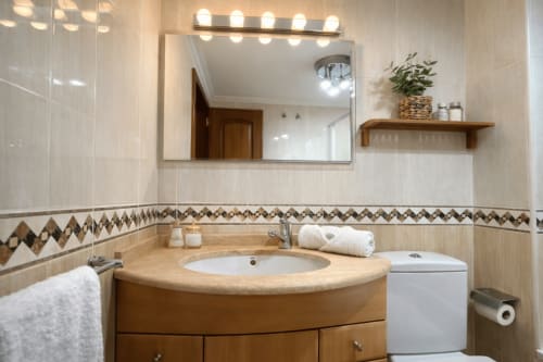 Baño moderno en apartamento Chuliña, Baiona con vanidad curva de madera, lavabo redondo, espejo grande con iluminación y