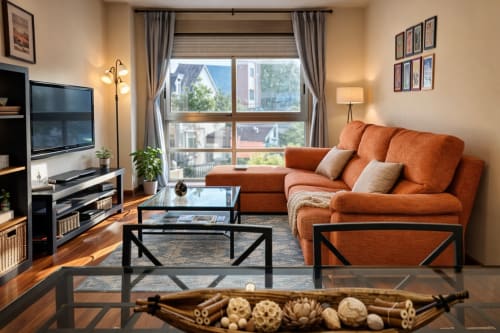 Moderno salón luminoso en Holibai Baiona con sofá seccional naranja, TV y amplias ventanas con vistas a la piscina