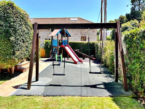 Parque infantil al aire libre con columpios y tobogán rojo en el apartamento familiar Holibai de Baiona, España