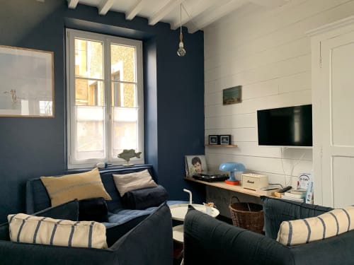 Séjour moderne au gîte La Maison sur le Quai : murs bleu marine, coussins rayés, TV écran plat, vue sur le port