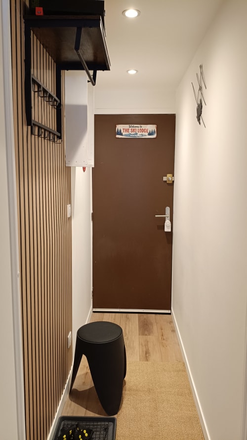Couloir étroit au Gîte des Gônes avec porte marron « The Ski Lodge », murs blancs, éclairage encastré et noir