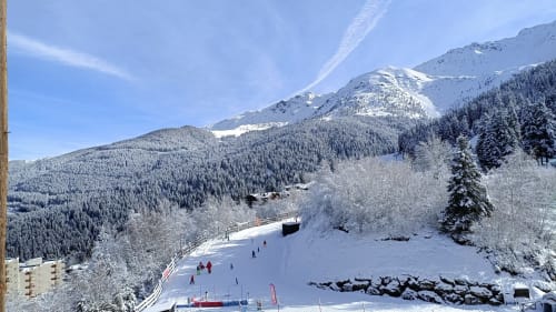 Paysage alpin enneigé avec station de ski, montagnes boisées et équipements de sports d'hiver près du Gîte des Gônes