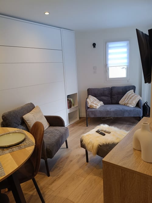 Salon moderne du Gîte des Gônes avec canapé gris rayé, fauteuil et rangements intégrés blancs