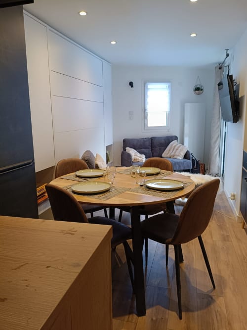 Salle à manger moderne du Gîte des Gônes avec table ronde en bois, chaises marron et séjour attenant à l'appartement de Feyzin