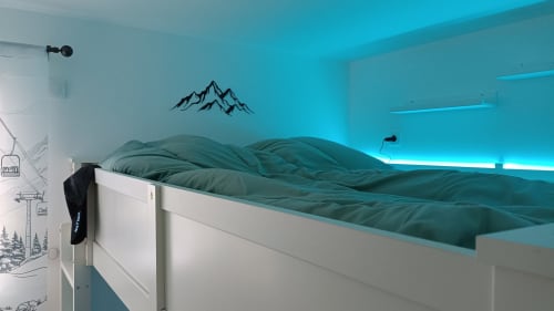 Chambre moderne du Gîte des Gônes avec literie bleu canard, art mural montagnard, éclairage d'accentuation turquoise et vue sur les montagnes