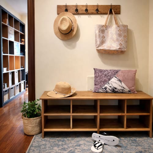 Entrada del apartamento de Baiona con banco de almacenamiento de madera, sombreros de paja, bolsa de tela estampada y cojines decorativos