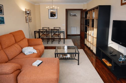 Amplio salón del apartamento Chuliña en Baiona con sofá naranja, comedor, televisor y mobiliario moderno