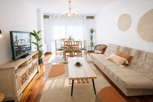 Luminoso salón moderno en apartamento de Baiona con sofá beige, mesa de comedor de madera, televisor y luz natural de las ventanas