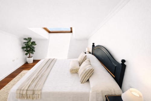 Dormitorio moderno y luminoso en dúplex Xanela, Baiona. Ropa de cama blanca, cama de estructura negra, planta en maceta, claraboya con vistas al mar