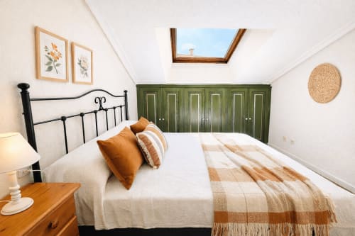 Dormitorio luminoso en Holibai de Baiona con cama de hierro negro, armario verde, tragaluces y vista al océano
