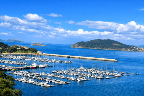 Marina de Baiona, España con veleros blancos e islas en aguas azules del Mediterráneo bajo cielo despejado