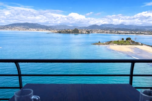 Vista de la costa de Baiona desde la terraza del apartamento con playa, montañas y pueblo costero bajo cielo azul