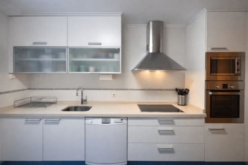 Cocina blanca moderna con electrodomésticos de acero inoxidable, isla con cocineta y campana extractora en apartamento A Son do Mar, Baiona