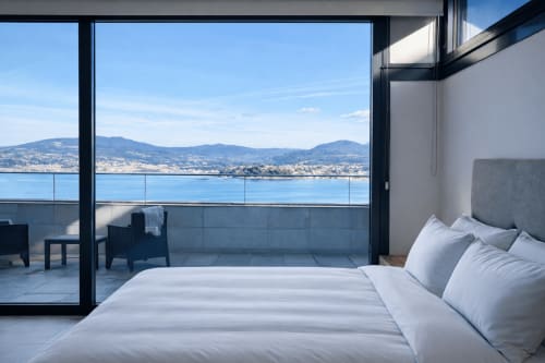 Lujoso dormitorio con ropa de cama blanca con vistas a la bahía de Baiona y las montañas, amplios ventanales que se abren a la terraza