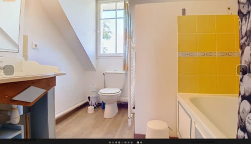 Salle de bains lumineuse avec carrelage jaune, douche, toilettes, vasque et fenêtre à l'appartement Loc'Maria de Belle