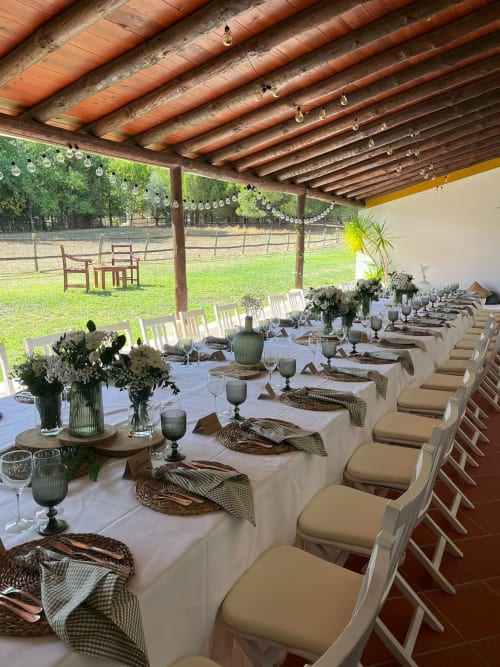 Elegant outdoor dining setup under wooden pergola at Quinta da Alcaidaria-Mór, Fátima, with long table, white chairs, floral