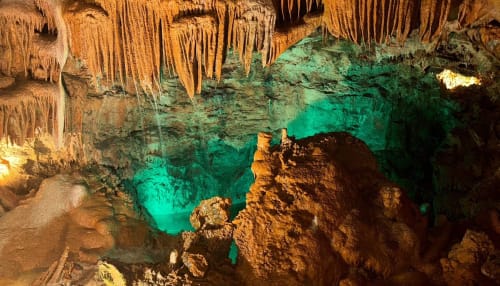 Underground cave with turquoise pool, stalactites, and brown limestone formations near Fátima, Portugal