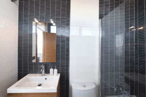 Baño moderno del apartamento Holibai Beiramar en Baiona con paredes de azulejos negros, lavabo blanco y ducha